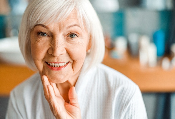 Older woman gently touching chin; smiling with dentures in Everett, WA