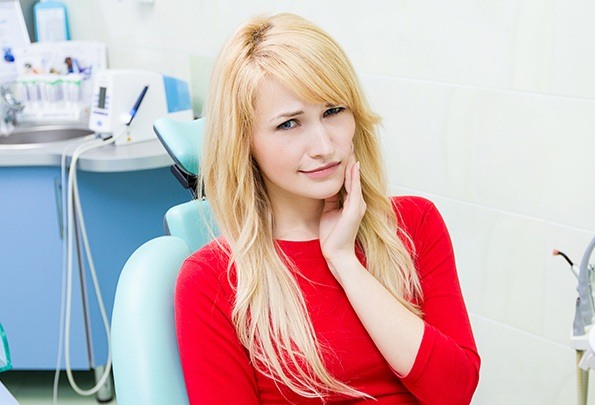 Woman in dental chair holding jaw