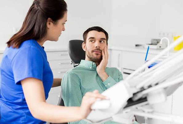 Man in dental chair holding cheek before emergency dentistry treatment