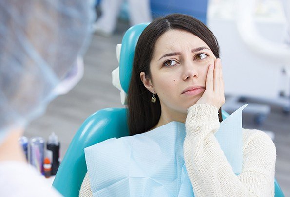 Woman in dental chair holding cheek before emergency dentistry