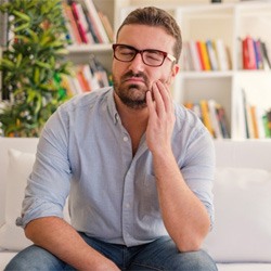 man sitting on couch holding his cheek in pain