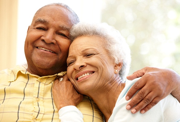 An older couple hugging and smiling while enjoying their new and improved smiles thanks to implant dentures in Everett