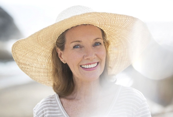 An older woman wearing a wide-brimmed hat smiling and showing off her new implant dentures