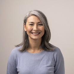 Woman with grey shirt and greying hair smiling with grey background