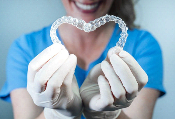 dental team member holding two clear aligners in the shape of a heart 