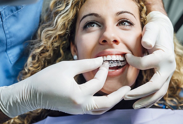 A dentist inserting an Invisalign aligner in a female patient’s mouth during her fitting