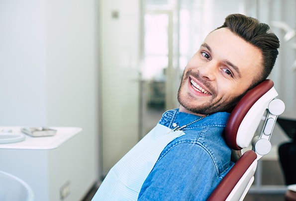 A young man with a beard sitting in the dentist’s chair smiling during a follow-up appointment after completing Invisalign