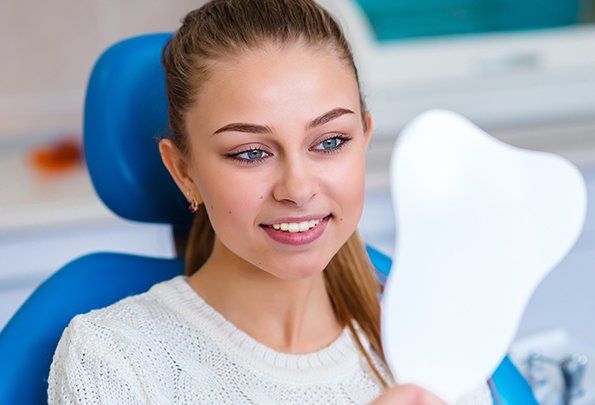 Woman looking at smile in mirror after Lumineers treatment