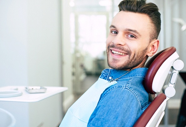 A young man wearing a denim shirt sits in a dentist’s chair and smiles in Everett