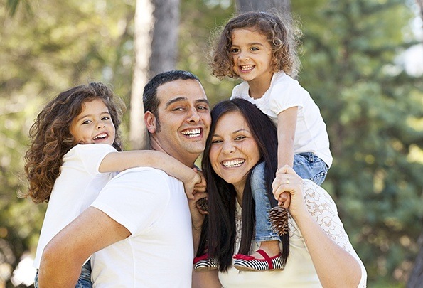 Smiling mother father and two children outdoors with healthy smiles after dental services