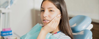 Young girl in dental chair holding jaw before emergency dentistry treatment