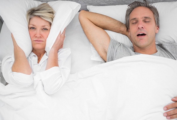 Woman covering ears while man snores due to sleep apnea in Everett, MA