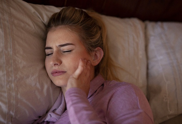 Woman in bed holding her jaw in pain