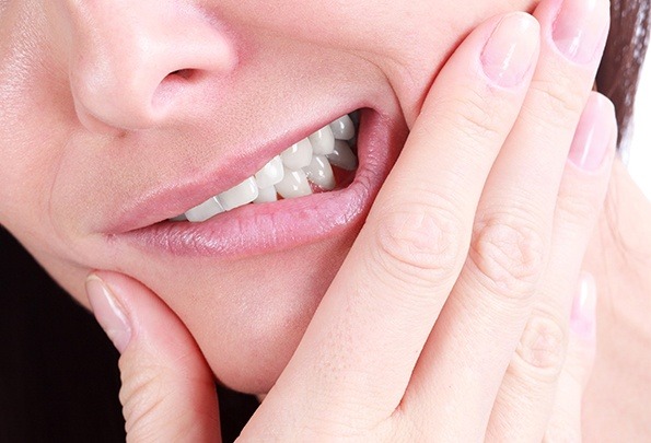 Closeup of person holding jaw in pain before wisdom tooth extraction