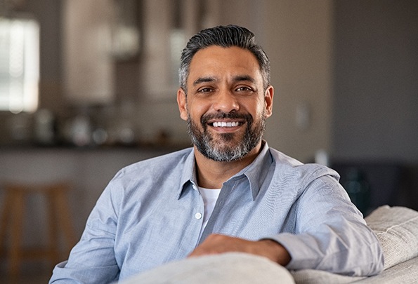 Man in blue shirt smiling while relaxing on couch