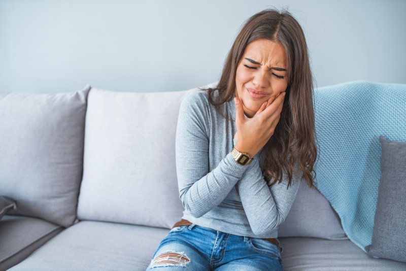 Woman with a toothache clutching her face on a couch