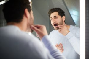 man looking at his gums in a mirror 