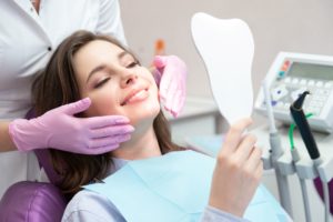 Woman in dentist chair looking in a mirror while the dentist stands behind her with purple gloved hands